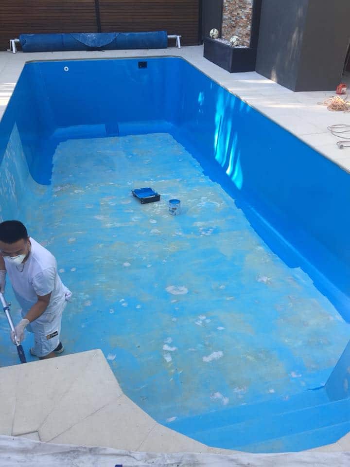Adelaide concrete pool mid-resurfacing — old yellow peeling surface, worker applying fresh blue coating system